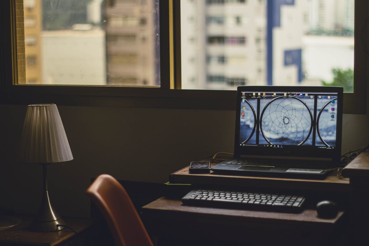 A tranquil home office setup with a laptop, lamp, and city view through the window.